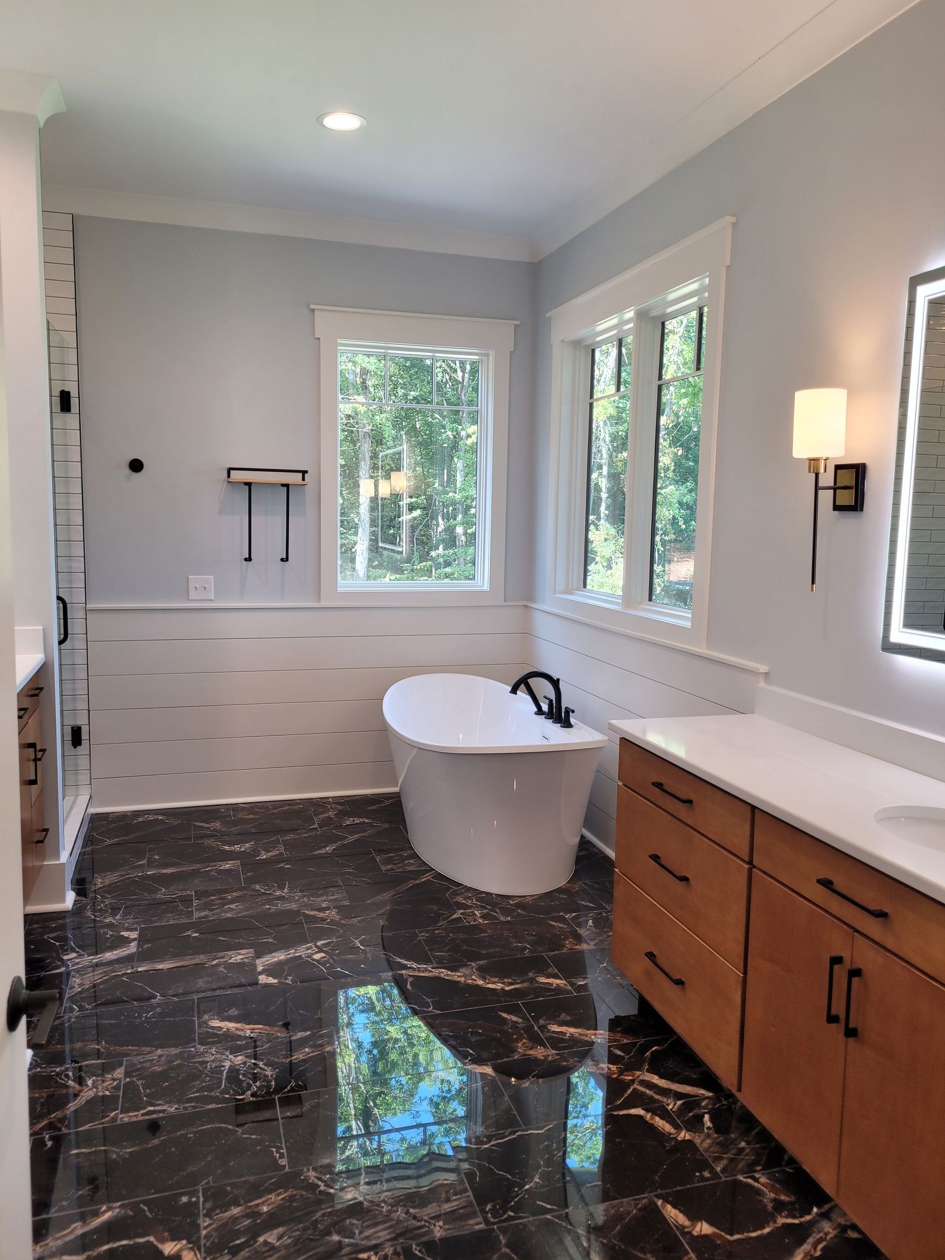Modern bathroom with black marble floor, white tub, light blue walls, and a large window.