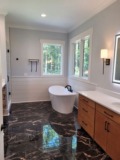 Modern bathroom with black marble floor, white tub, light blue walls, and a large window.