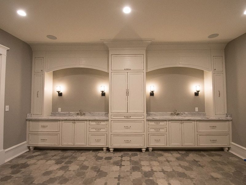 Built-in white vanity with arched sections, sinks, and a central cabinet, with sconces and overhead lights.