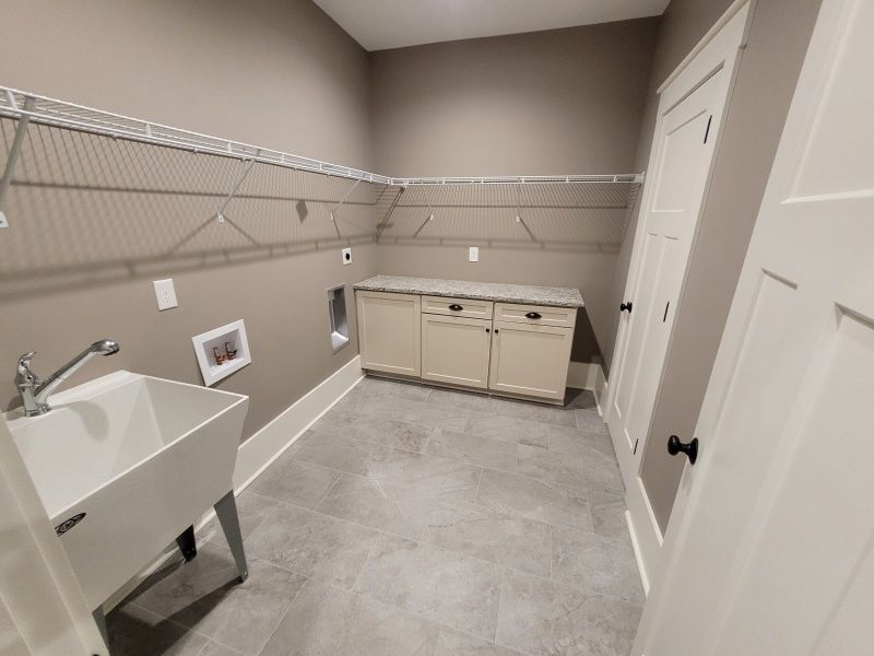 Laundry room with a utility sink, cabinets, shelving, and a large closet. Gray tile, tan walls, and white trim.