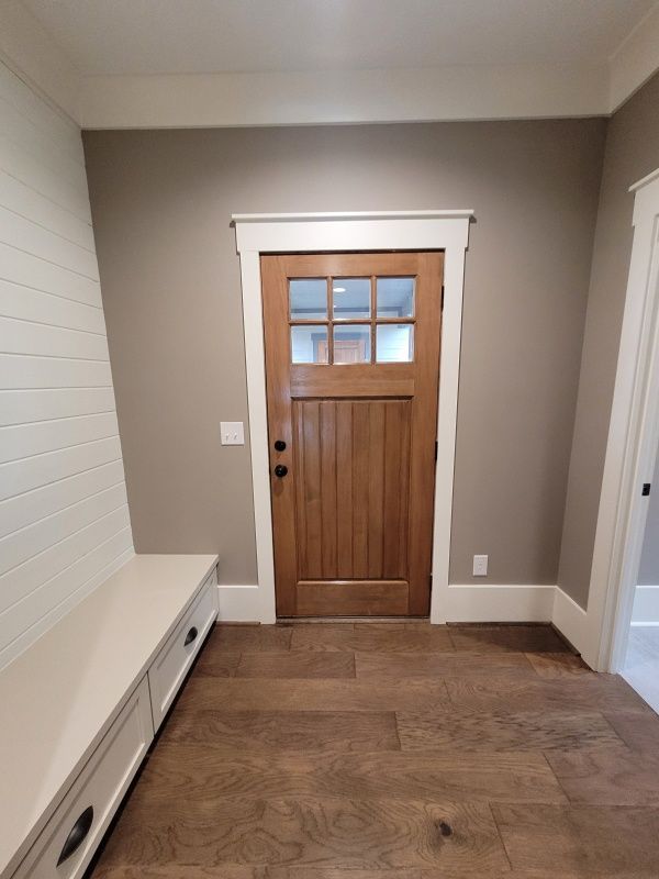 Entryway with wooden door, brown walls, white trim, bench, and wood floor.