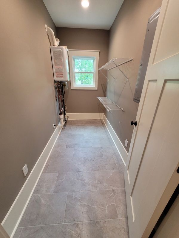 Narrow laundry room with gray tile floor, brown walls, and white trim; door open, small window.