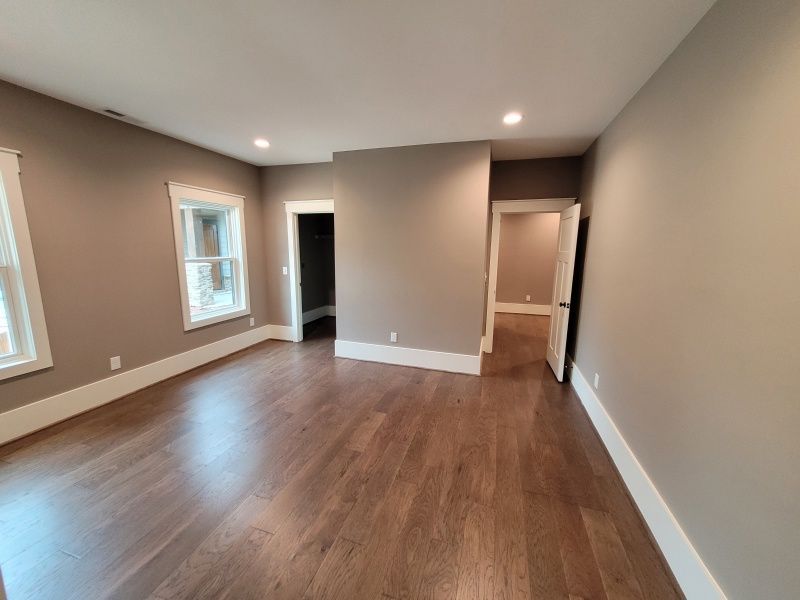 Empty bedroom with hardwood floors, tan walls, white trim, and doorways.