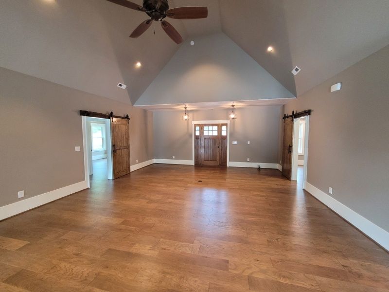 Spacious room with wood floors, high ceiling, barn doors, and a wooden front door.