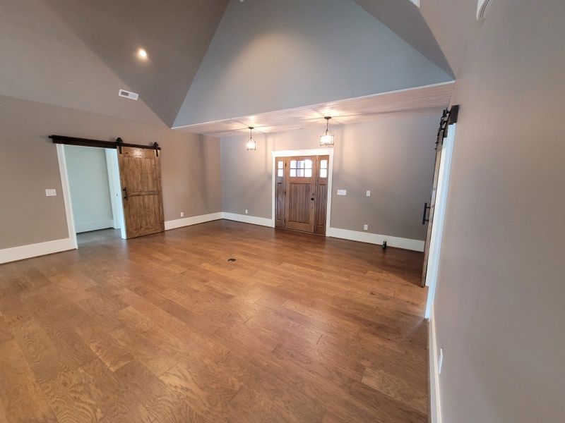 Spacious room with wood floors, gray walls, and wooden barn door. Door with glass panes.