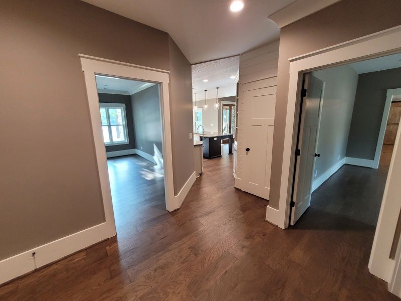 Hallway with three doorways leading to different rooms, hardwood floors, brown walls and white trim.