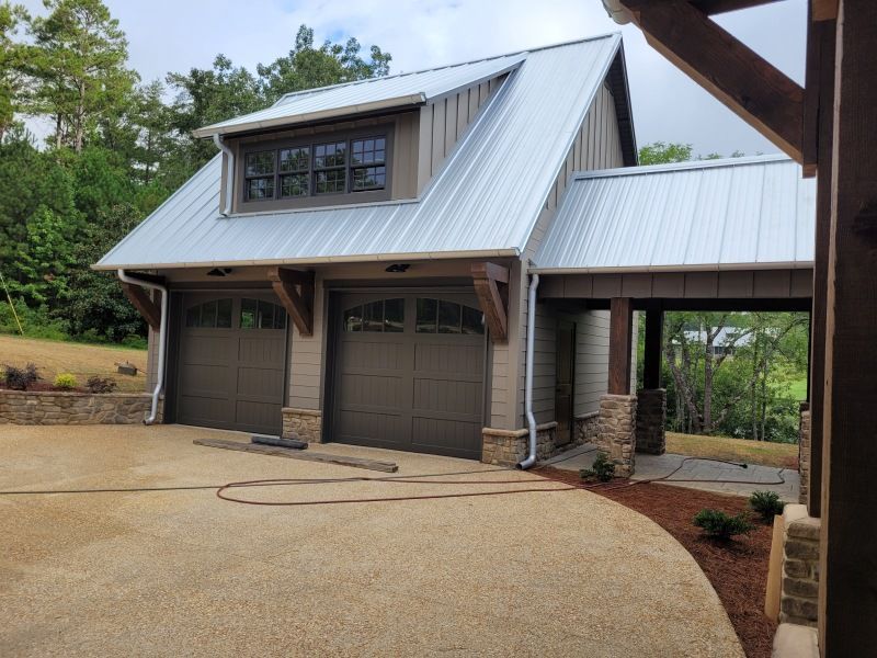 Garage with metal roof, brown doors, and wooden beams, set in a gravel driveway.