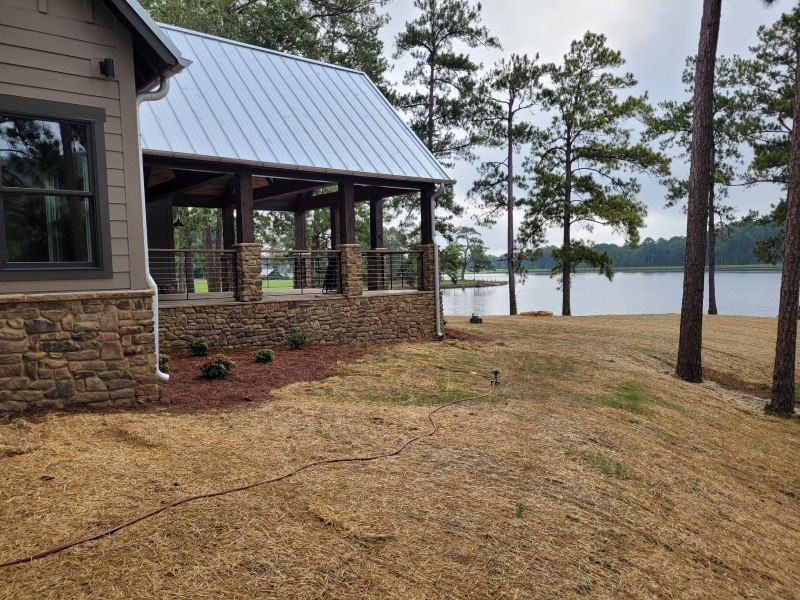 A house with a stone facade and an open pavilion overlooking a lake with trees.