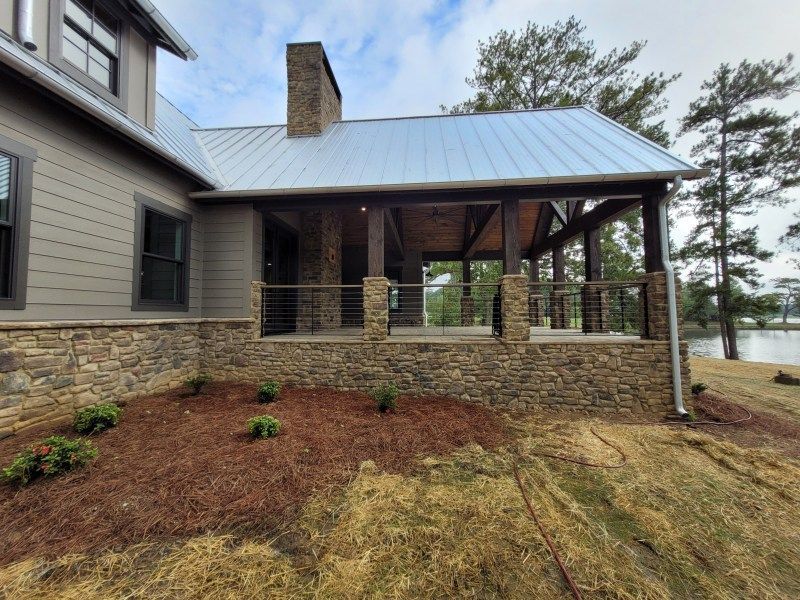 A house with a stone foundation and a covered porch, lake view. Brown siding and a metal roof.