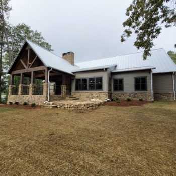 A modern house with a covered porch, stone and gray siding, metal roof, and brick chimney.