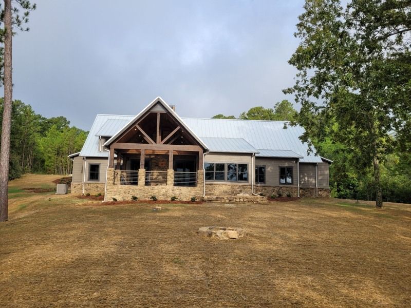 Modern gray house with a metal roof, wooden porch, and stone accents on a grassy hill.