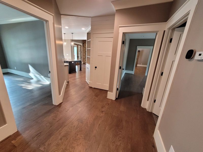 Hallway with hardwood floors, three doorways, and a white cabinet.