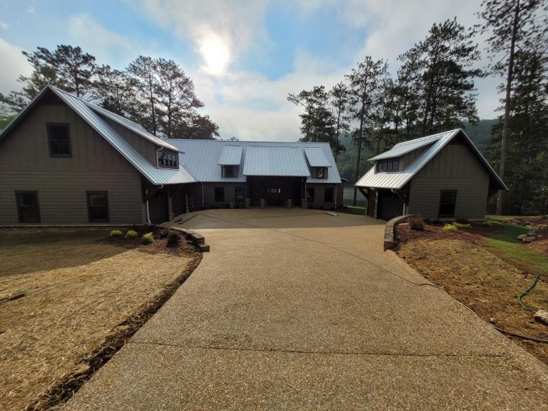 A gray house with a long driveway, surrounded by trees, on a cloudy day.