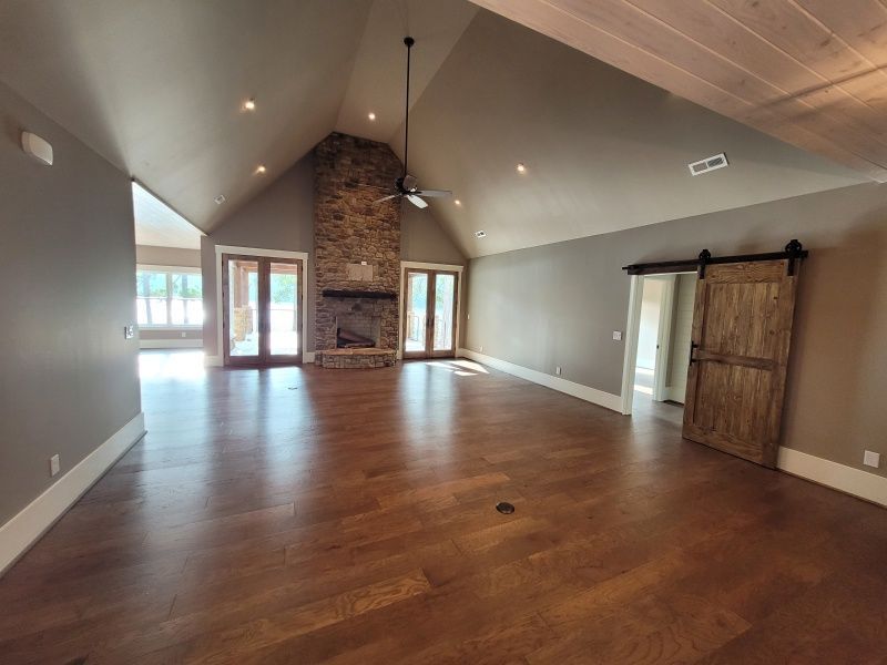 Spacious room with hardwood floors, stone fireplace, vaulted ceiling, and a barn door.