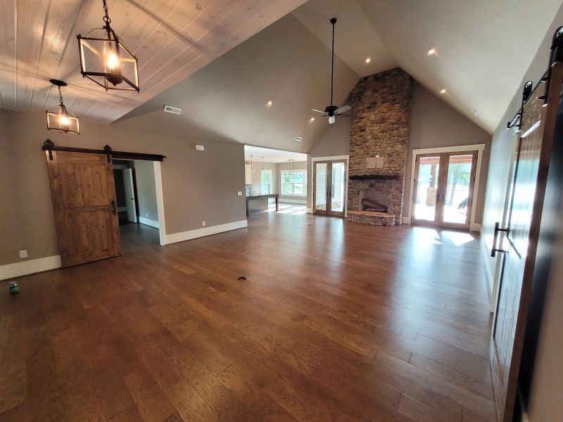 Spacious living room with wood floors, vaulted ceiling, stone fireplace, and large windows.  Barn door.