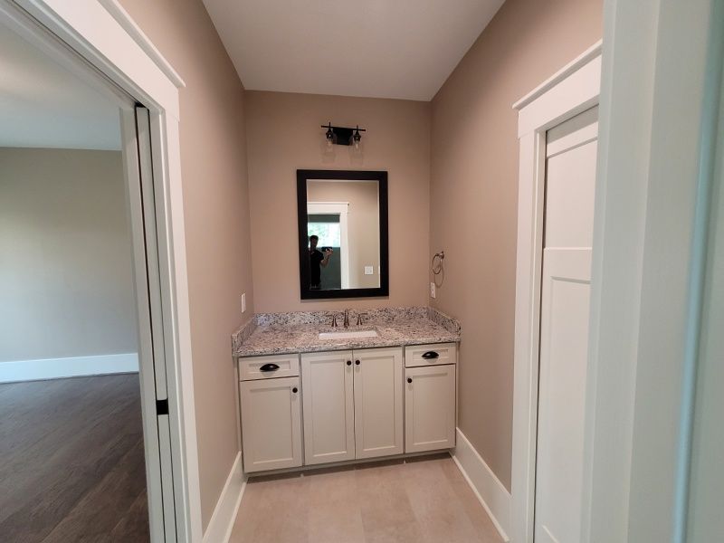 Powder room with white vanity, granite countertop, and black-framed mirror. Neutral walls and light flooring.