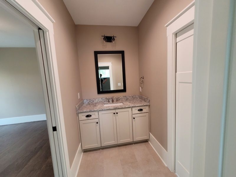 Small bathroom with vanity and mirror; white cabinets, tan walls, stone countertop.