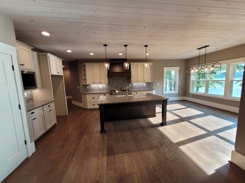 Open-concept kitchen with light cabinets, dark island, wood floors, and a water view through windows.