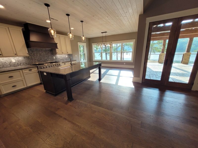 Kitchen with dark island, cream cabinets, wood floors, and lake view through sliding glass doors.