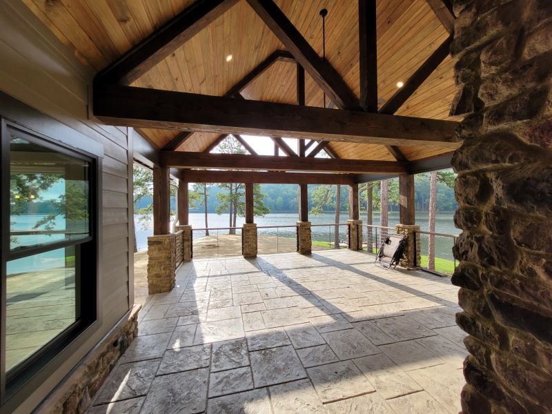 Covered patio overlooking a lake with stone columns and textured concrete floor.