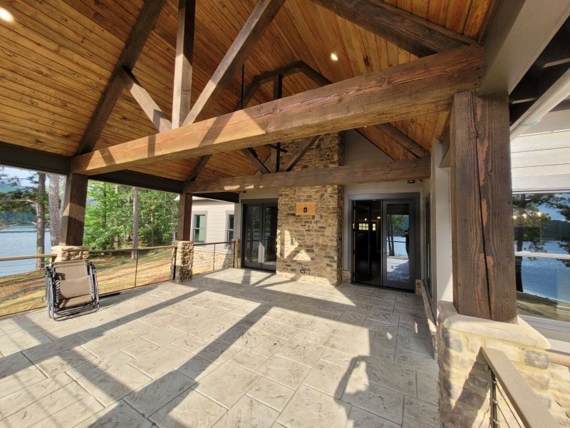A covered patio with exposed wood beams, stone fireplace, and lake view.