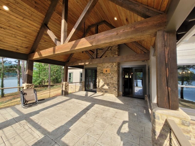 Covered patio with wood beams and stone fireplace overlooking a lake.