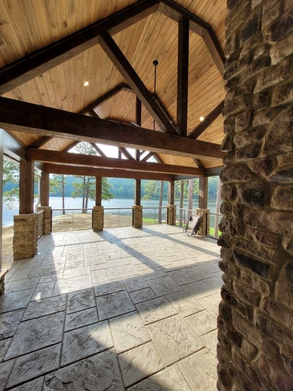 Open-air screened porch overlooking a lake. Features stone pillars and flooring, wooden ceiling beams.