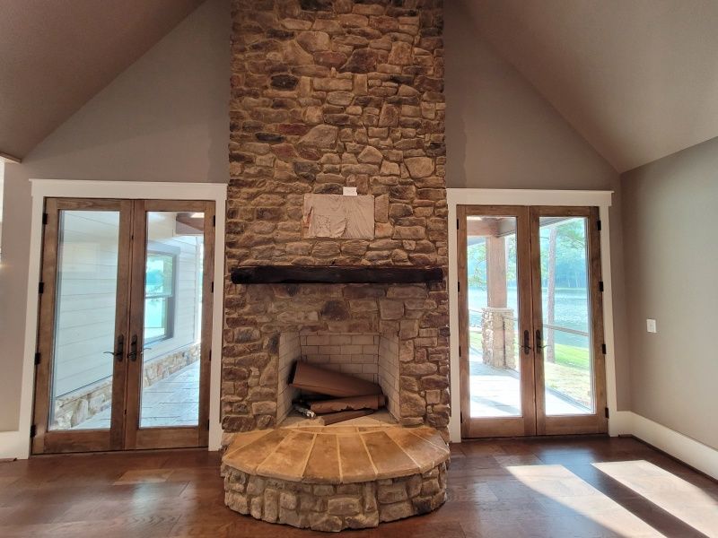 Stone fireplace with a wooden mantel, flanked by glass doors in a large, empty room.
