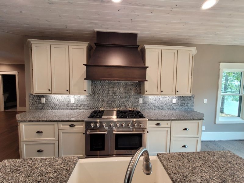 Cream cabinets surround a stainless steel range and range hood in a kitchen with granite countertops.