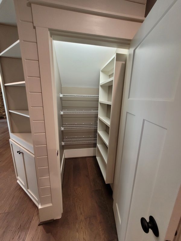 Built-in white shelves surround a narrow hallway to a walk-in pantry. Door is open.
