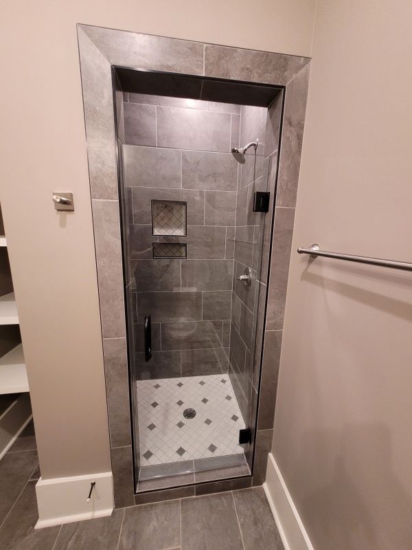 Gray tiled shower with glass door, black hardware, and white and gray patterned floor.