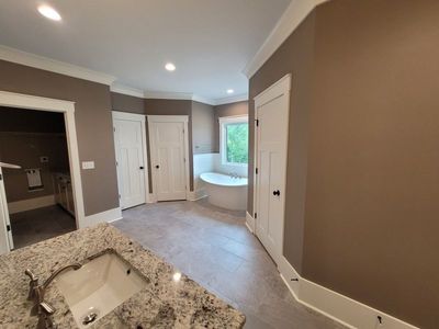 Spacious bathroom with a granite countertop, oval tub, and brown walls. White trim and doors.