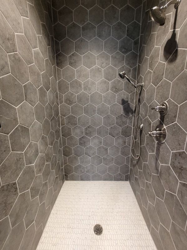 Gray hexagon-tiled shower with white floor. Silver shower fixtures.