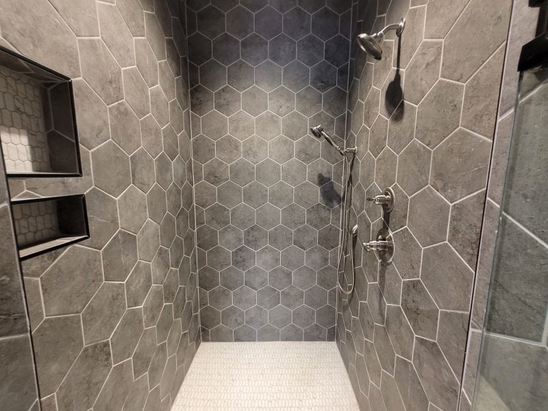 Gray tiled shower with hexagon pattern, shower fixtures, and built-in shelf.