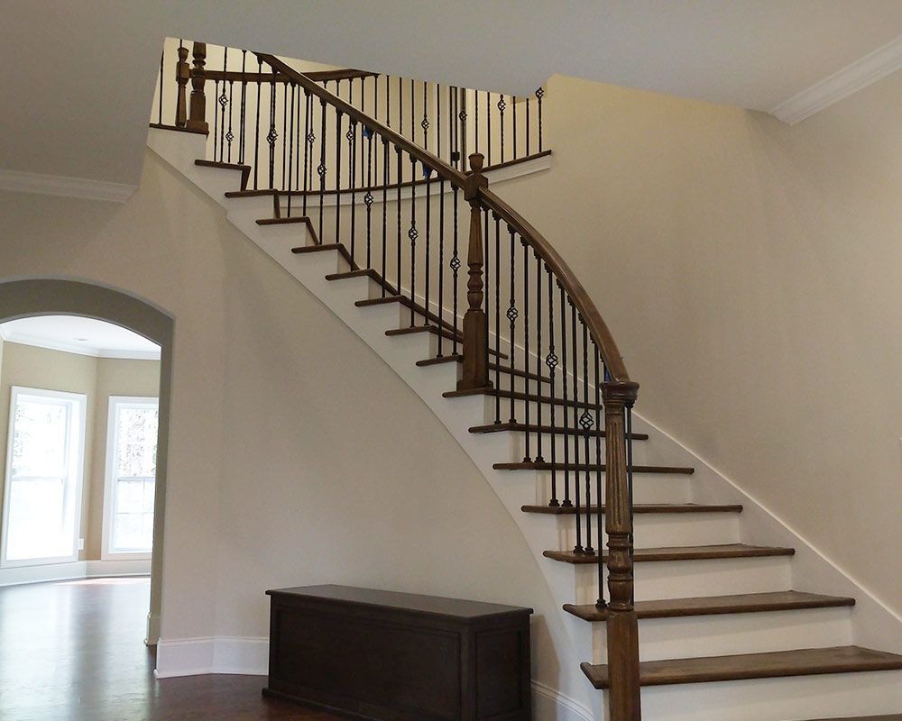 Staircase with dark wood railing and steps, dark chest at the base. Beige walls, archway to the left.