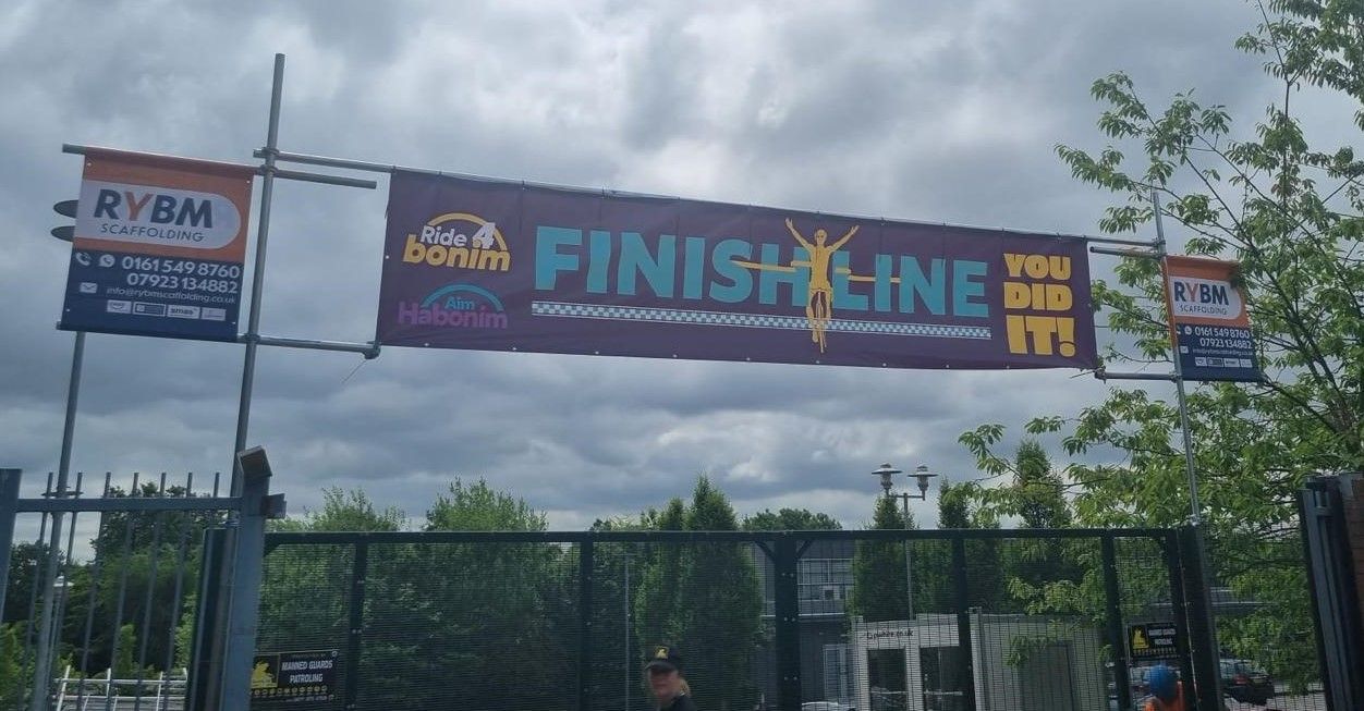 The banner of a Charity Bike race finish line is displayed, titled Bike4Bonim, This 100Km ride raises funds for a local special educational needs school, RYBM was a sponsor of this initiative, and RYBM management have actively partook in previous 100Km rides for this institute.