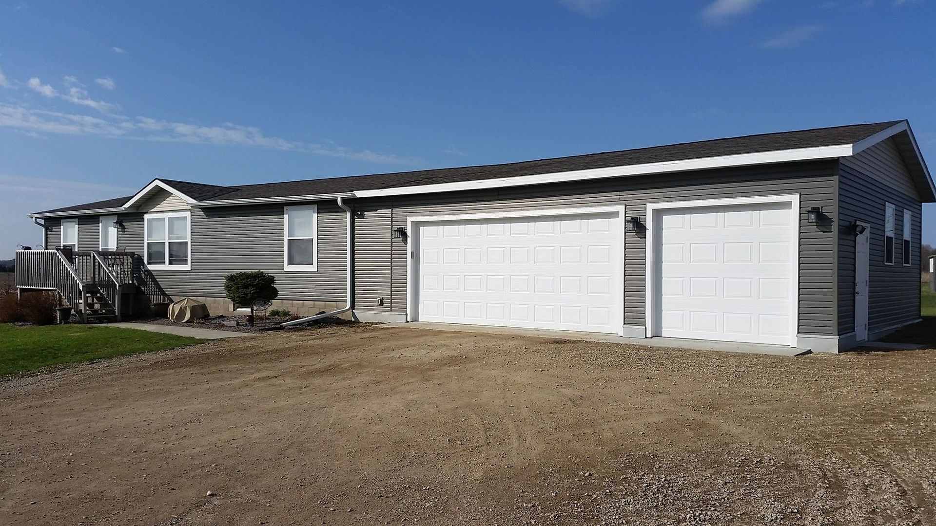 A large house with two garage doors is sitting on a dirt road.