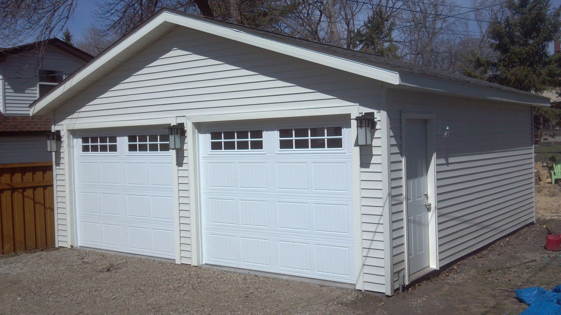 A white garage with two garage doors and a wooden fence