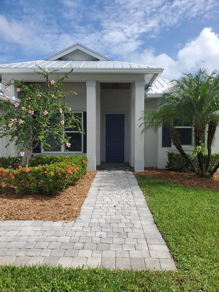 House exterior with a paved walkway, blue door, and landscaping under a blue sky.