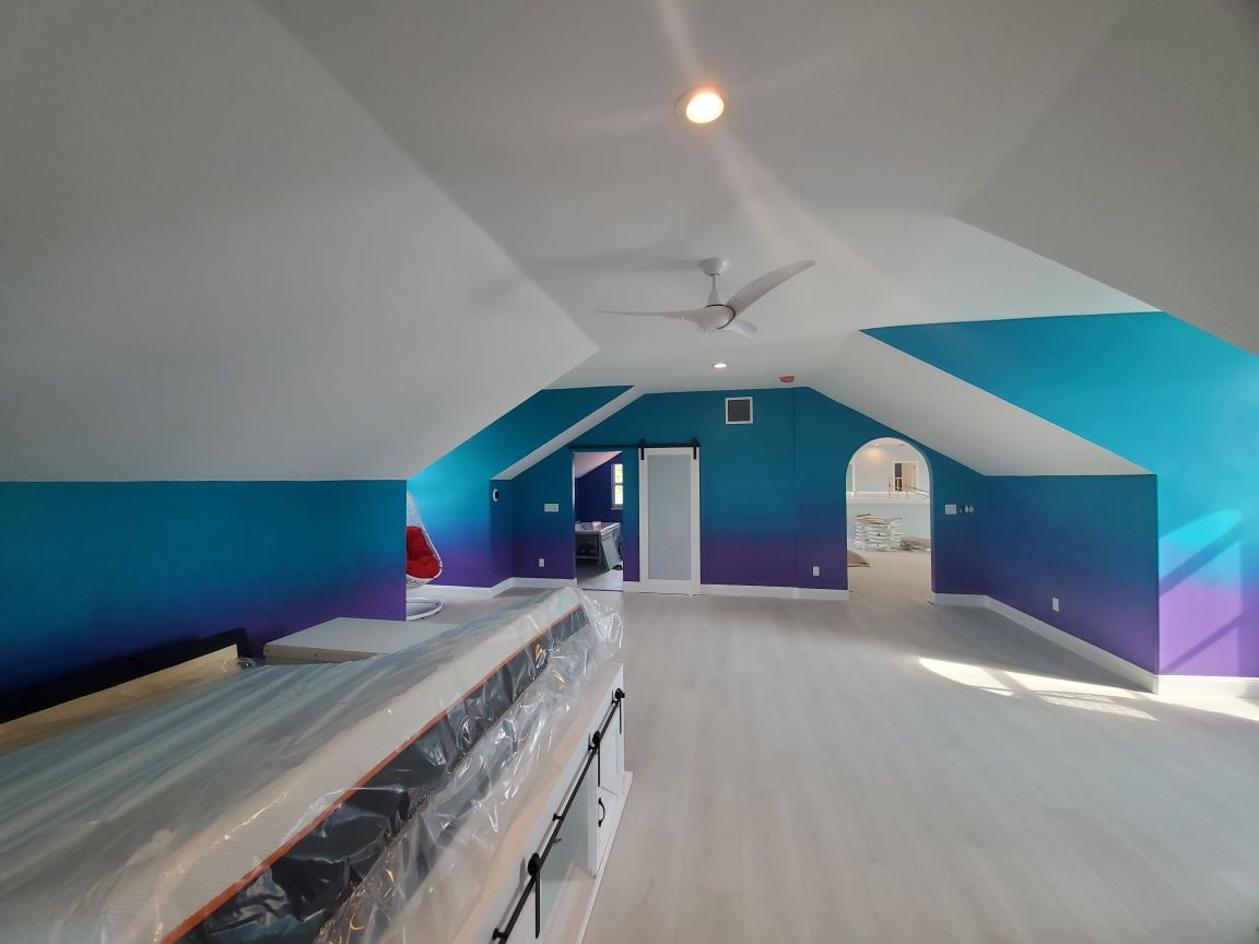 Loft bedroom with gradient blue and purple walls, white ceiling, light wood floors, and new mattresses.
