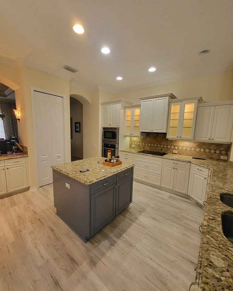 Kitchen with gray island, light cabinets, tan countertops, and light flooring.