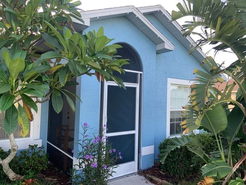 Blue house with screened porch, surrounded by green plants.
