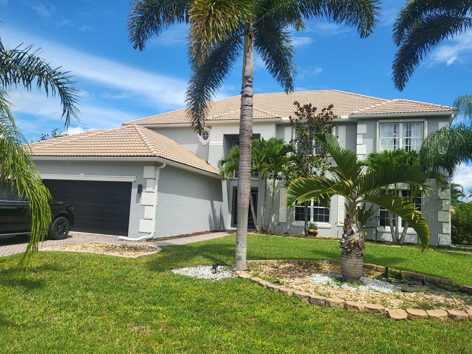 Gray house with palm trees, green lawn, and a blue sky.