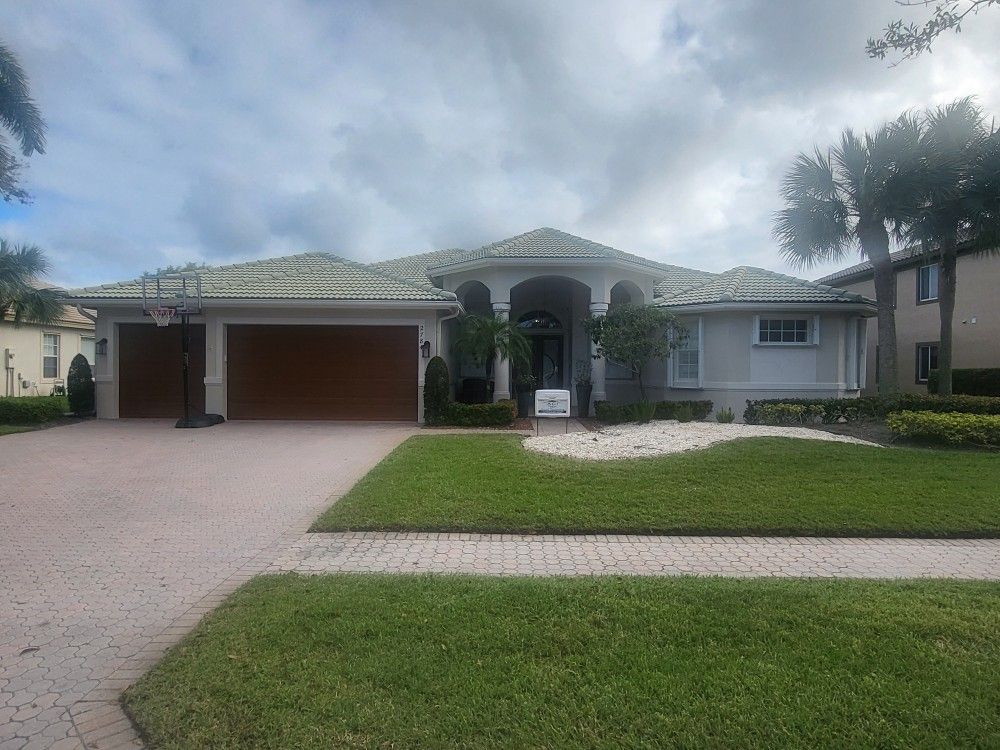 A light gray house with brown garage doors, green roof, and a green lawn.