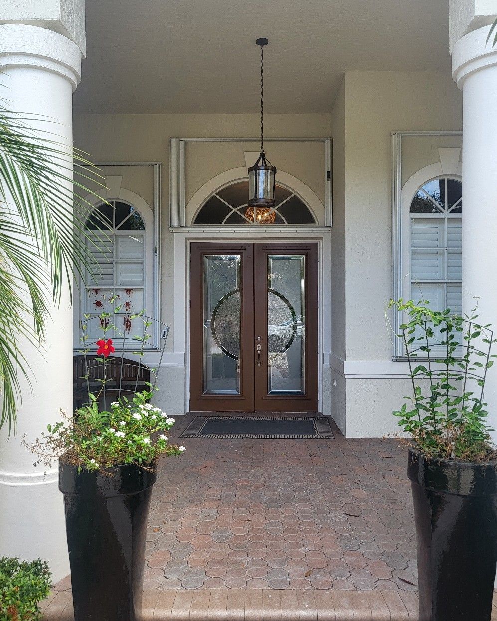 Brown double doors with sidelights and arched transom under a hanging lantern; flanked by columns and planters.