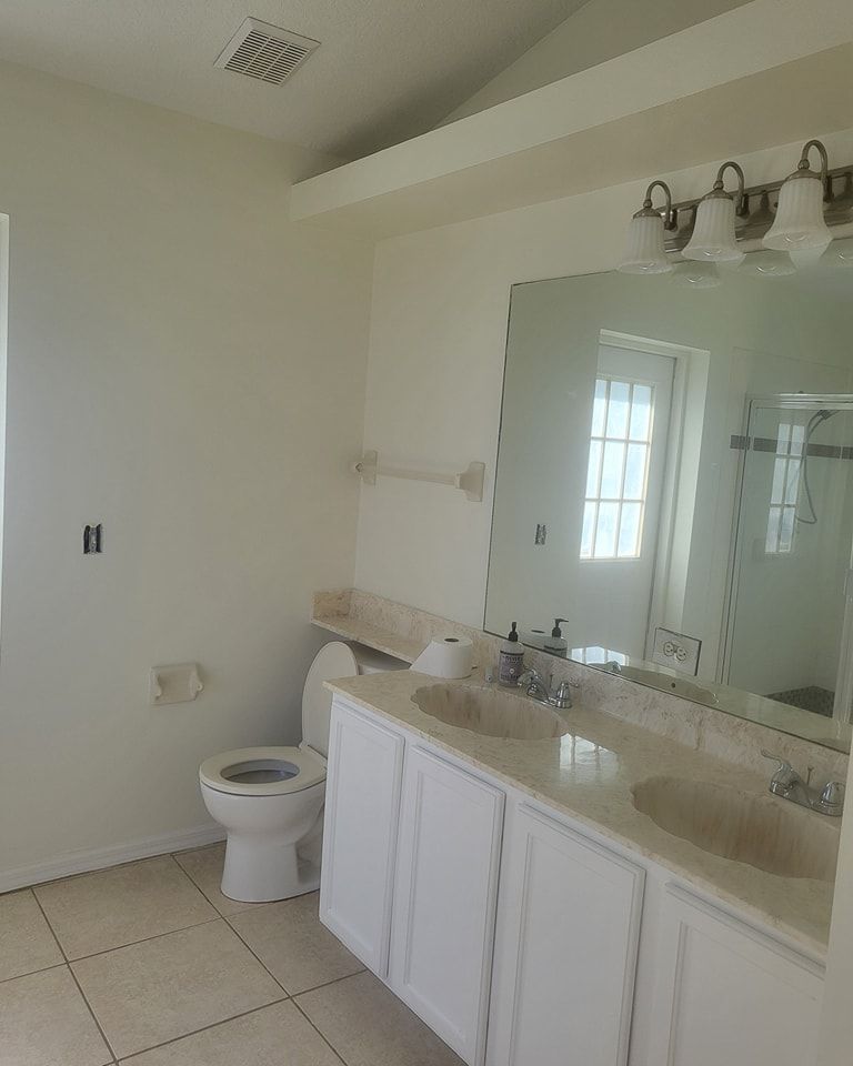 Bathroom with white vanity, toilet, and beige tile floor. Large mirror reflects window.