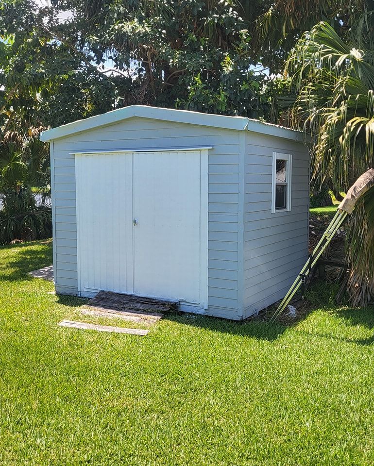 A blue shed with white doors and a small window on a grassy lawn.