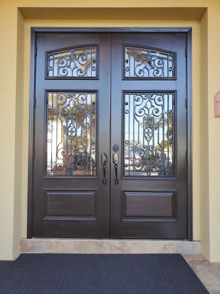 Double brown doors with wrought iron detail and glass panes, set in a light-colored building facade.