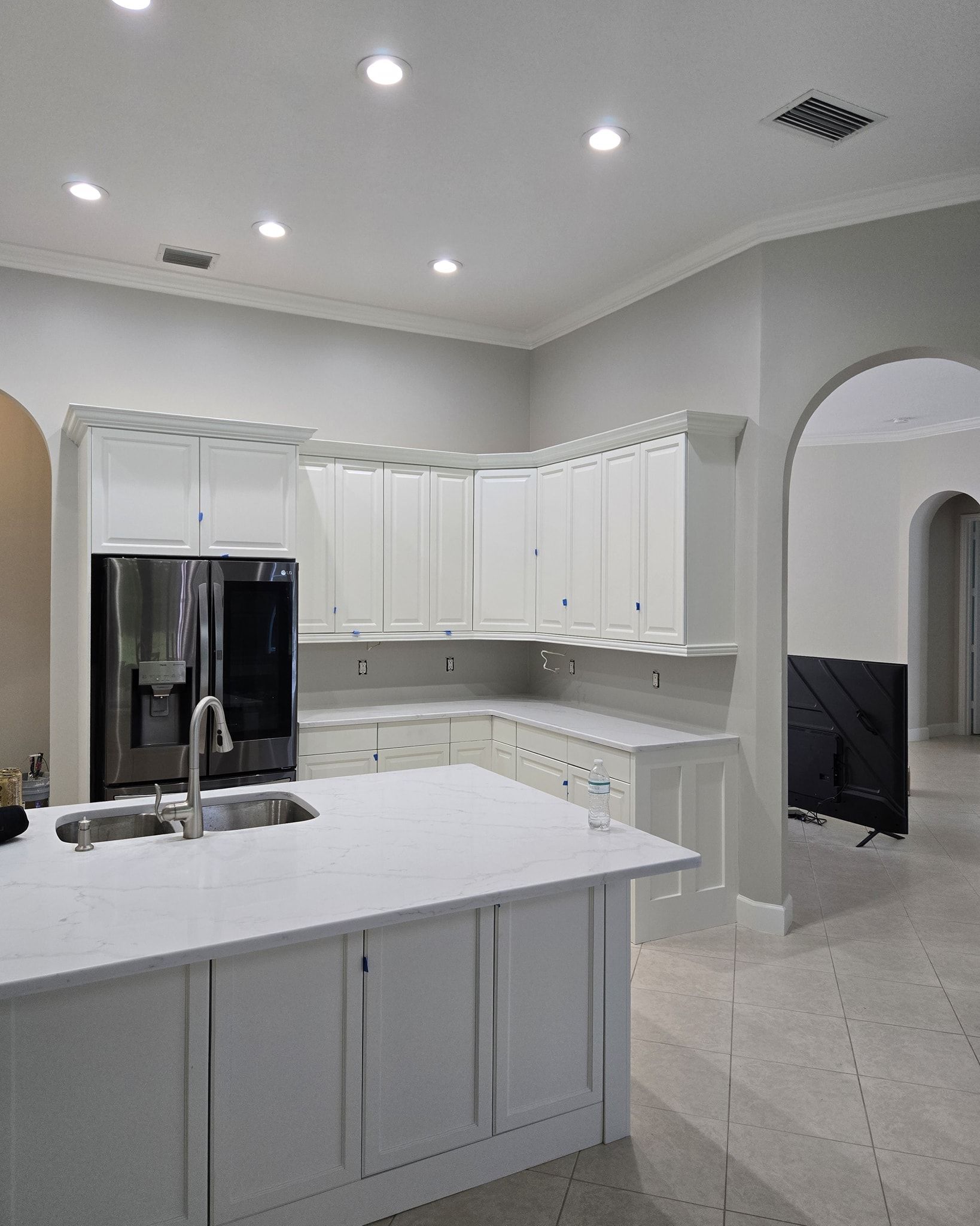 White kitchen with island, cabinets, and a refrigerator, with recessed lighting and an arched doorway.