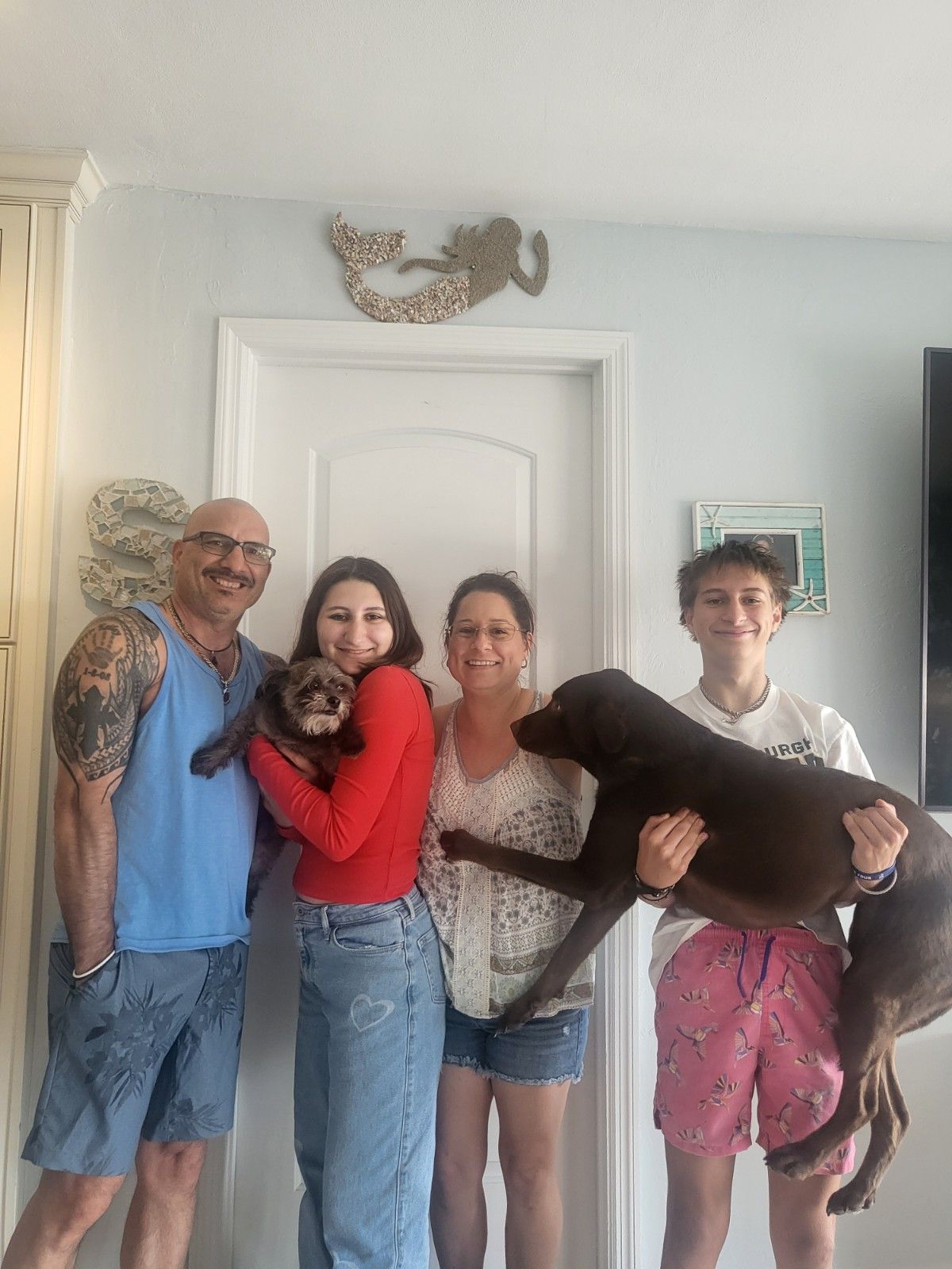 Family with pets: man holding a dog, woman holding an otter, by a door, smiles.